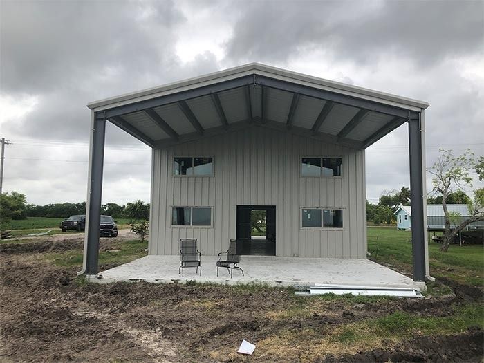 Two-story metal building with a large front porch, grey siding, and dark steel frame under a cloudy sky.