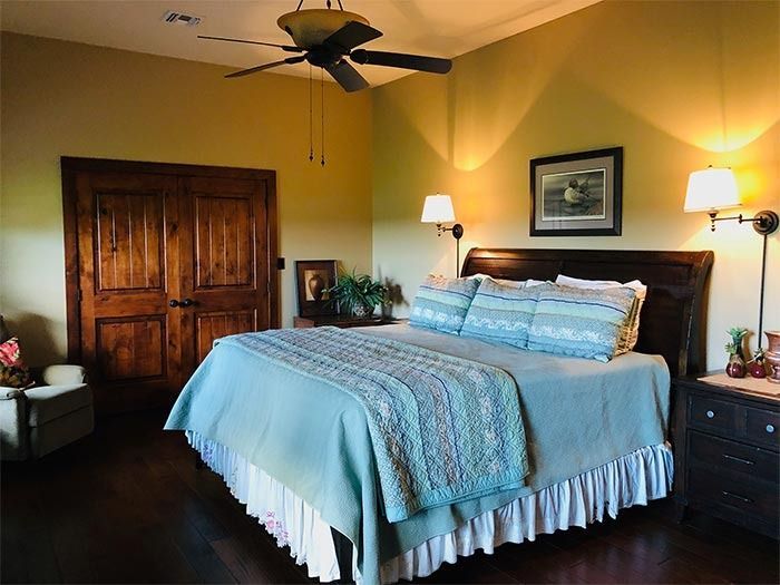 A cozy bedroom featuring a queen bed with blue bedding, a dark wood headboard, matching nightstands, and French doors.