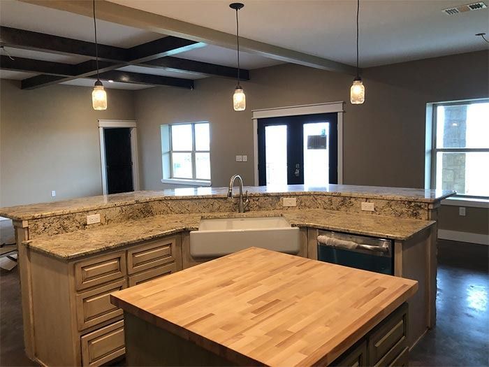 Kitchen island with wood countertop, granite counters, farmhouse sink, and three pendant lights under dark ceiling beams.