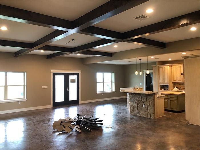 An open-concept living area with dark stained wood ceiling beams, a stone-front kitchen island, and a rustic windmill art.