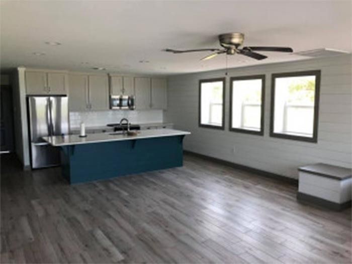 A modern kitchen with a dark blue island, stainless steel appliances, gray cabinets, and light gray wood floors.