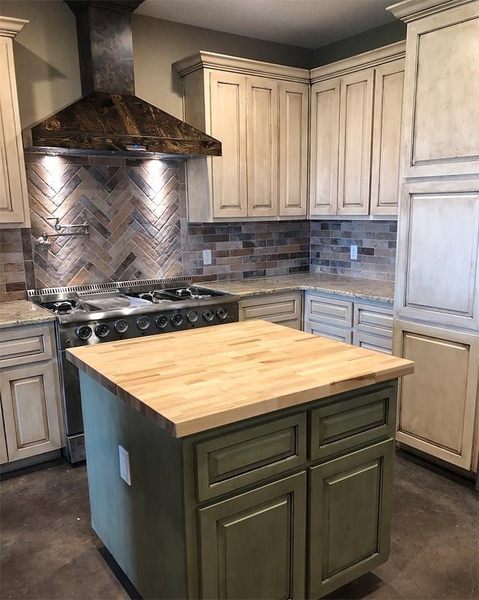A kitchen with distressed white cabinets, a green island with a butcher block top, and a brick backsplash.