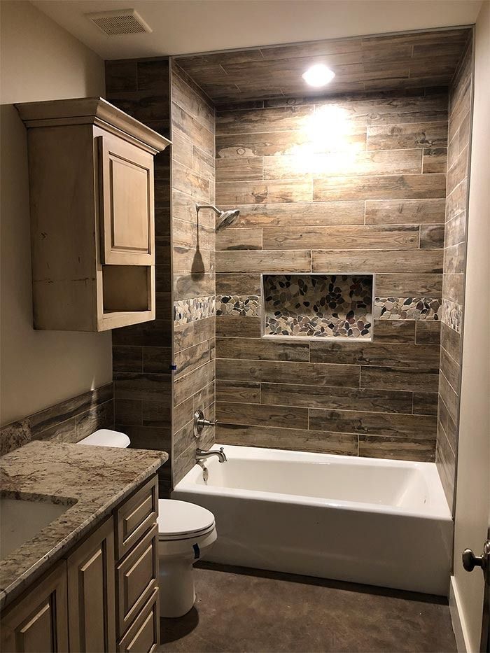 A bathroom featuring a wood-look tiled shower area with a recessed niche, a white bathtub, toilet, and vanity with stone.
