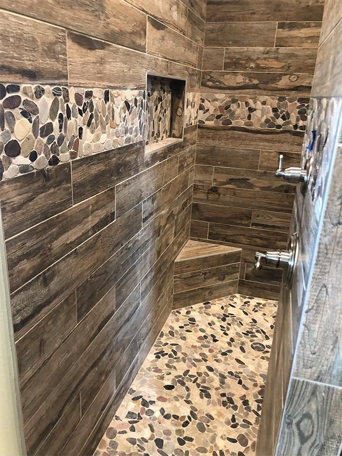 A shower with wood-look tile walls, a pebble floor, a small built-in corner seat, and a horizontal pebble mosaic accent.