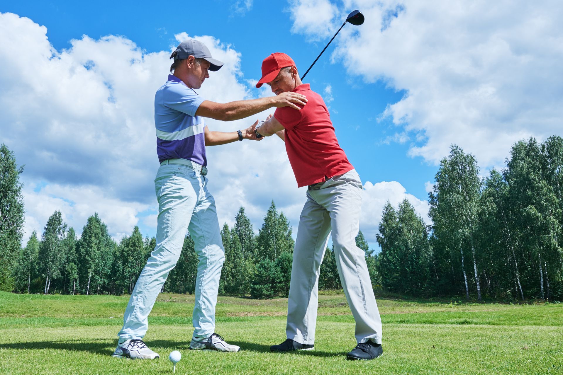 A man is teaching another man how to play golf on a golf course.
