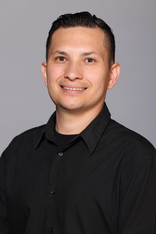 Smiling person in a black shirt against a gray studio background