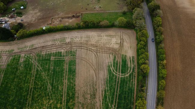 An aerial view of a road bordering a green field with tractor tire marks forming a clear U-turn pattern.