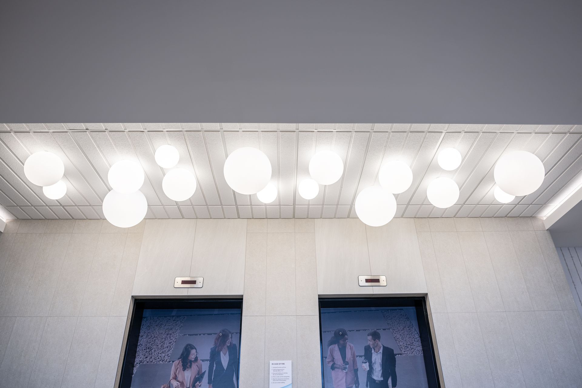 A couple of elevators in a building with lights hanging from the ceiling.