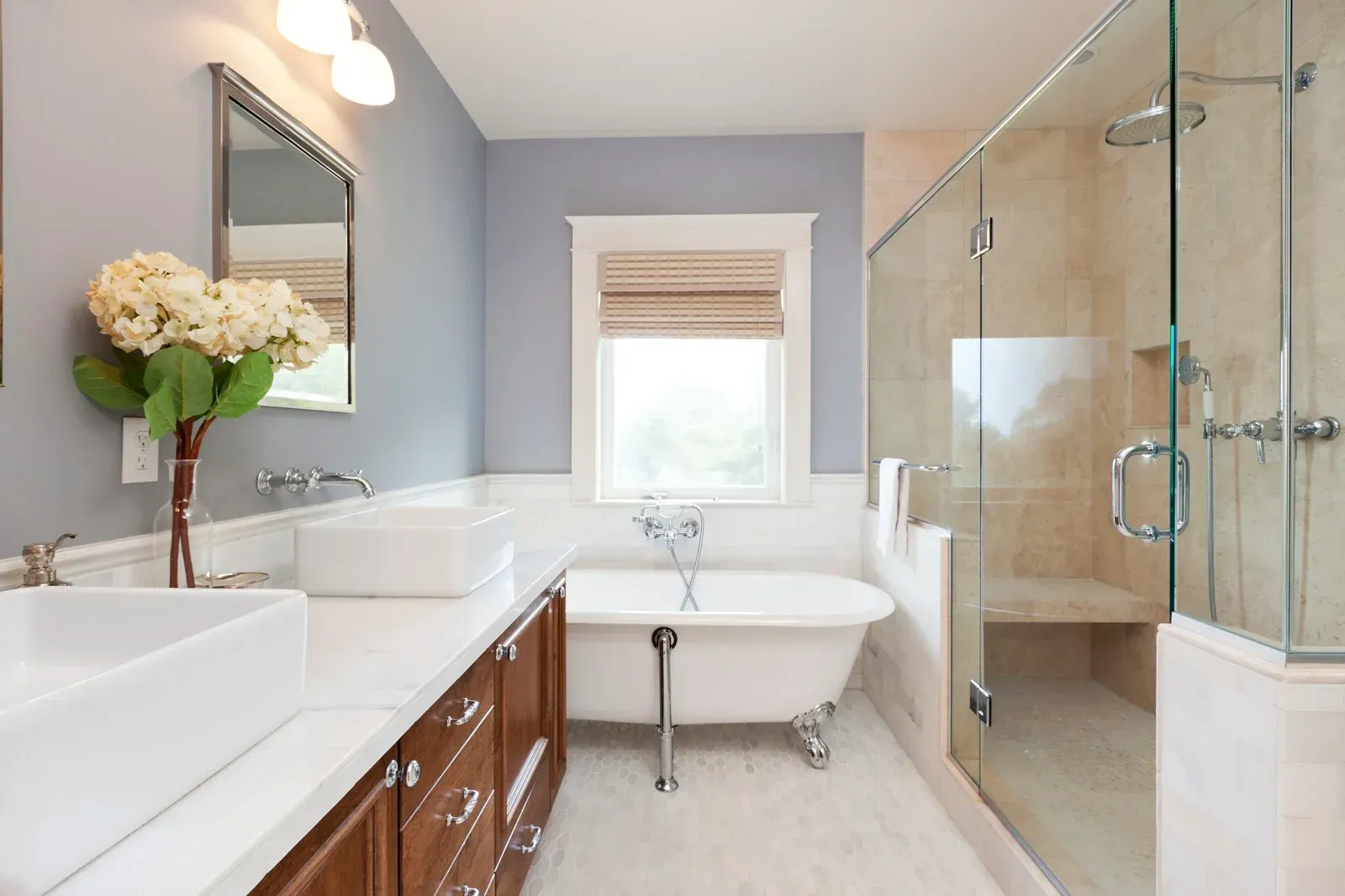 Bathroom with a claw-foot tub, glass shower, double sinks, wooden vanity, and blue walls.
