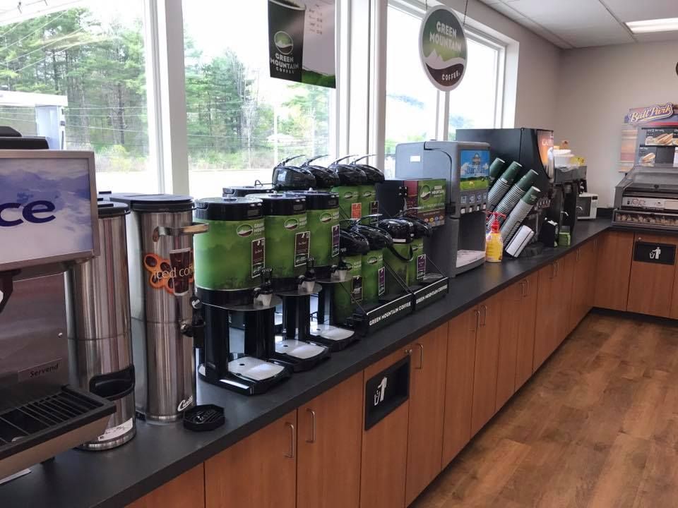 Coffee and beverage station inside a convenience store, featuring various dispensers and cups on a countertop.