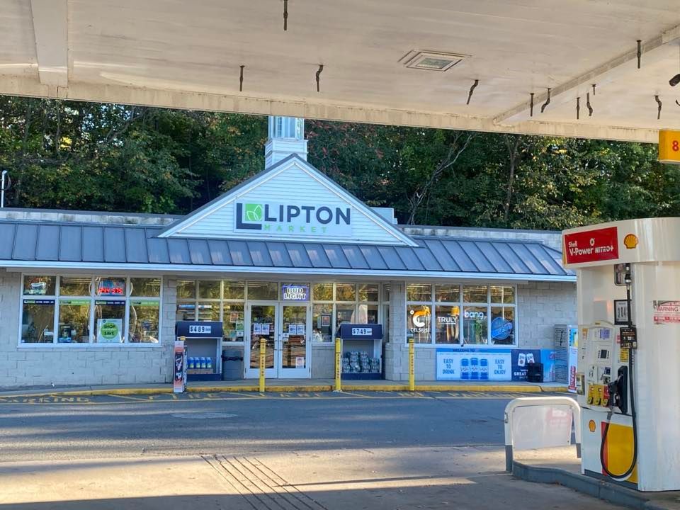 Lipton Mart gas station with white and gray exterior, trees in the background, and gas pumps in the foreground.