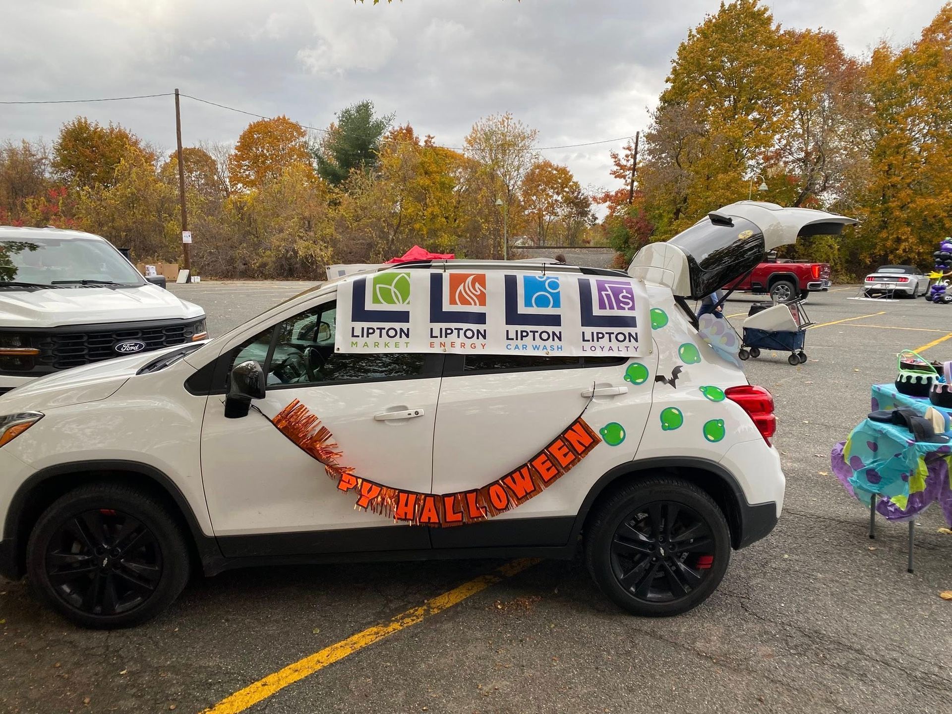 White car decorated for Halloween with trunk open and banner.