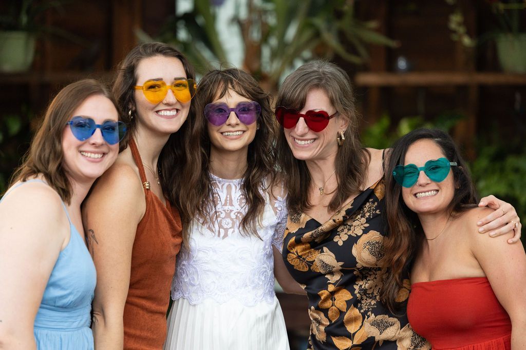 Five friends smiling in colorful sunglasses, posing together outdoors.