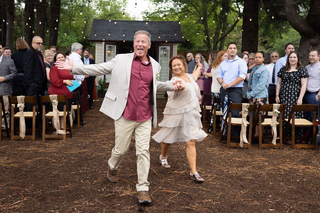Couple dancing down an outdoor aisle at a backyard wedding, guests seated and watching.