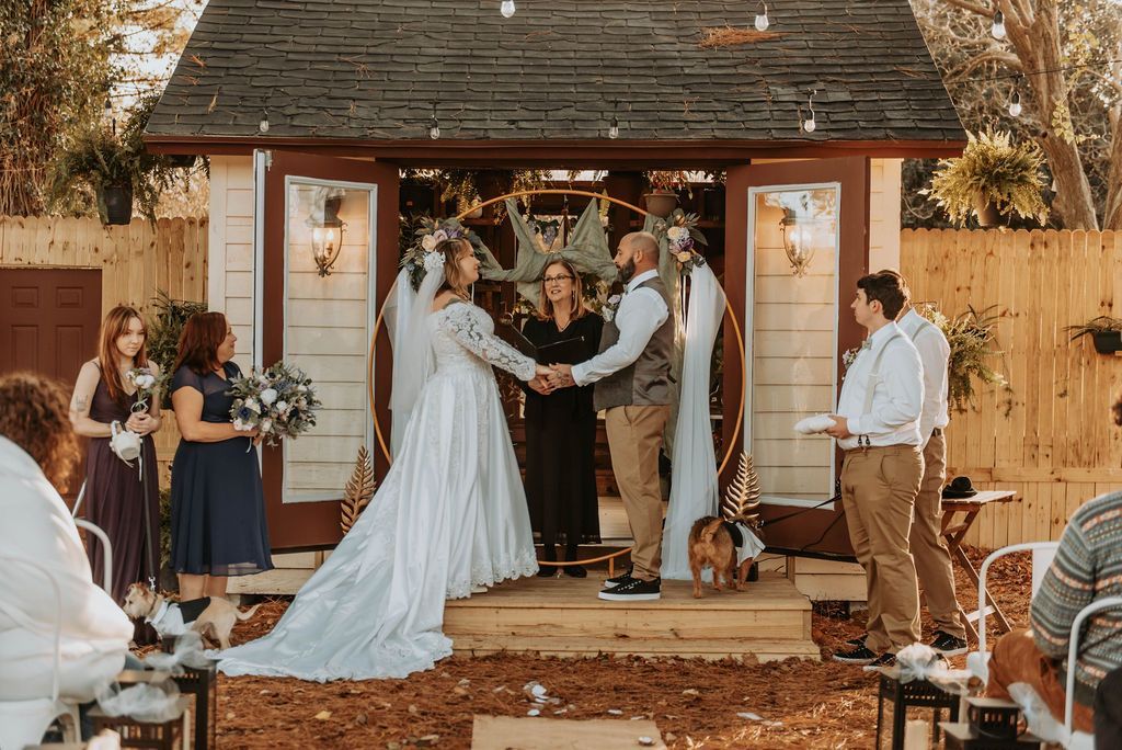 a bride and groom are holding hands during their wedding ceremony in front of a small shed .