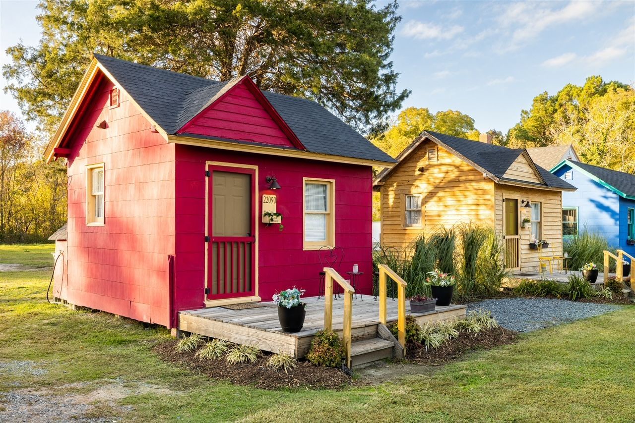 a red house is sitting in the middle of a field next to a yellow house .