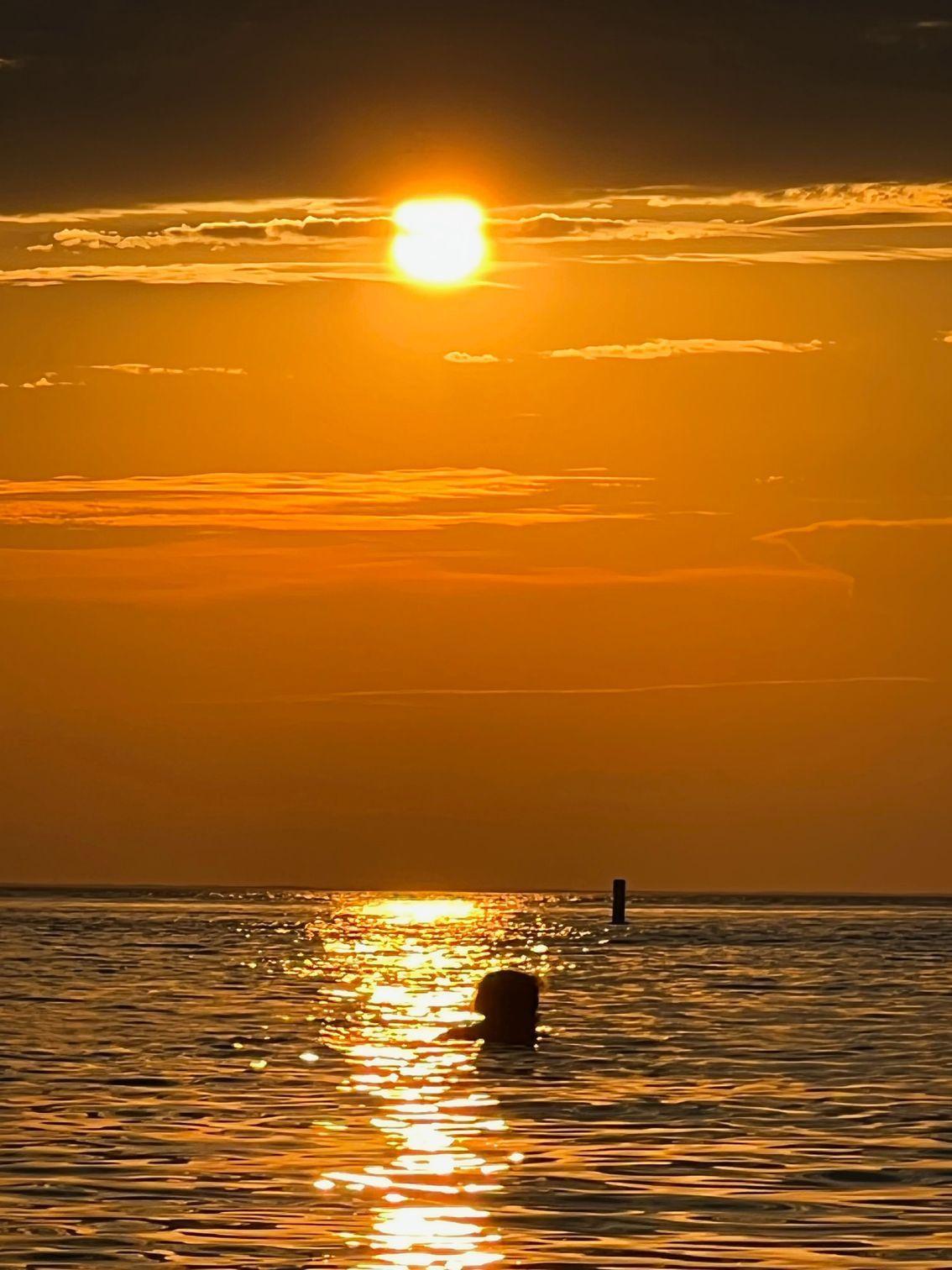 the sun is setting over the ocean with a buoy in the water .