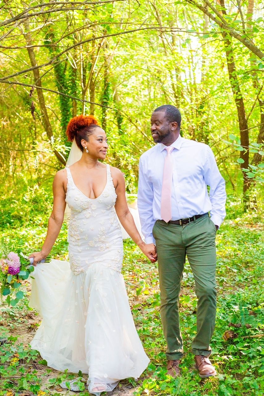 a bride and groom are walking through the woods holding hands .