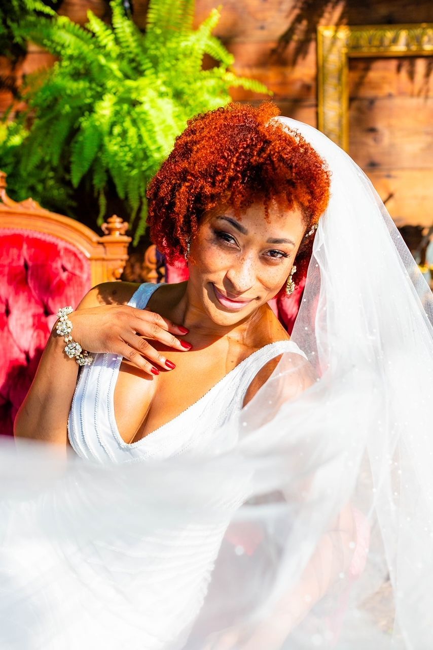 a woman in a wedding dress and veil is sitting on a red chair .