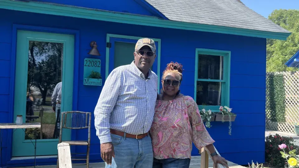 A man and a woman are standing in front of a blue house.