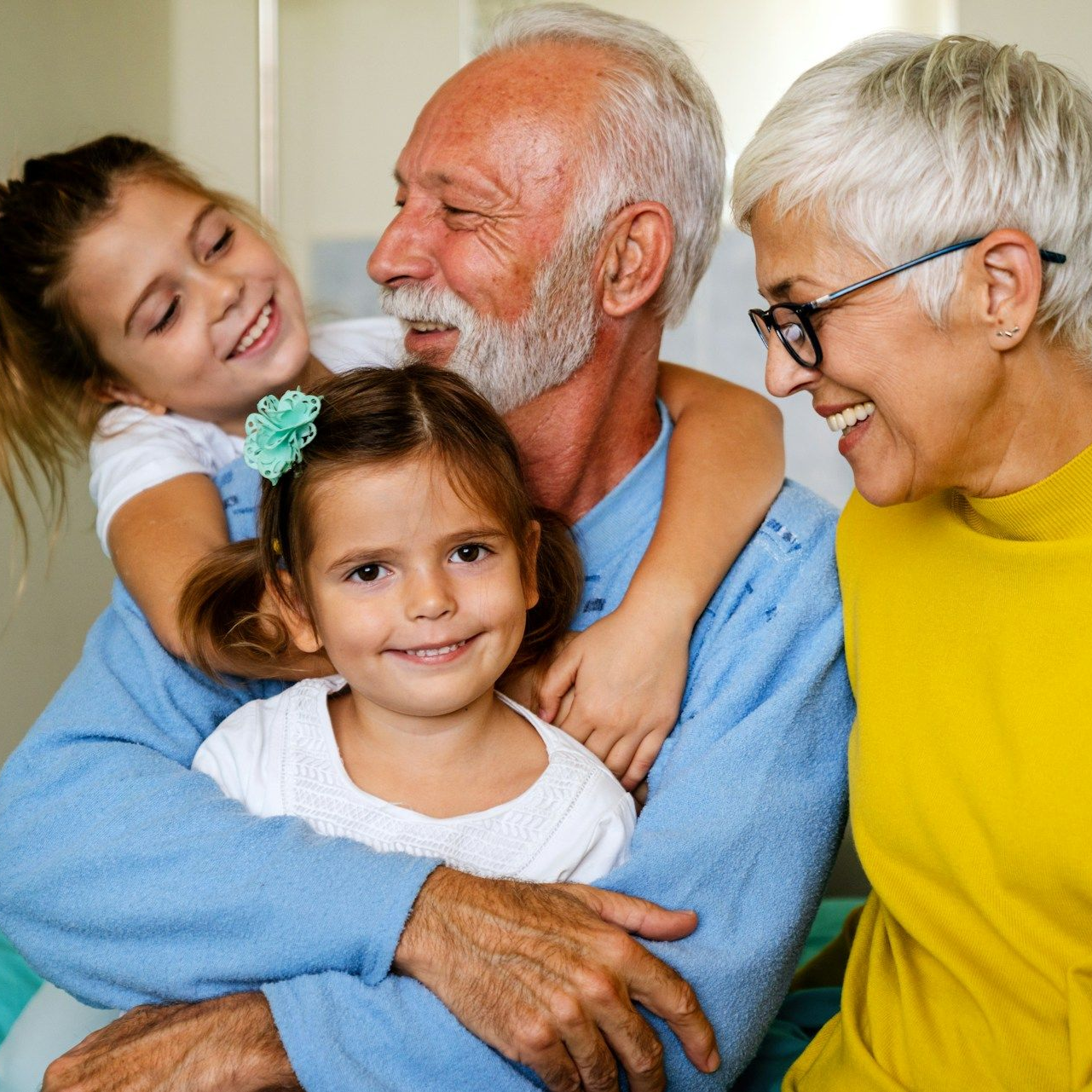 Grandfather smiling, hugging two young children; grandmother smiles beside him.