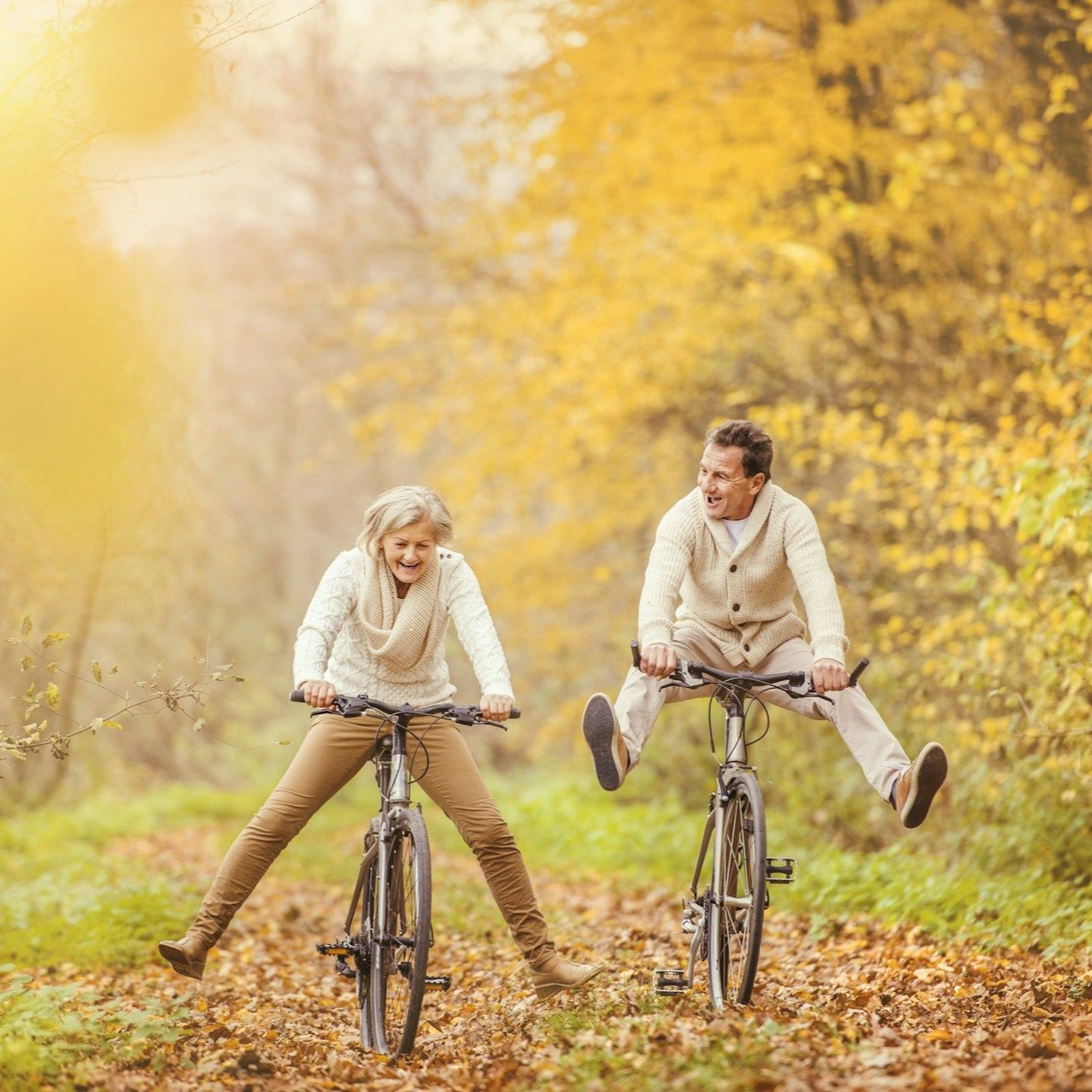 Couple joyfully riding bicycles through fall foliage.