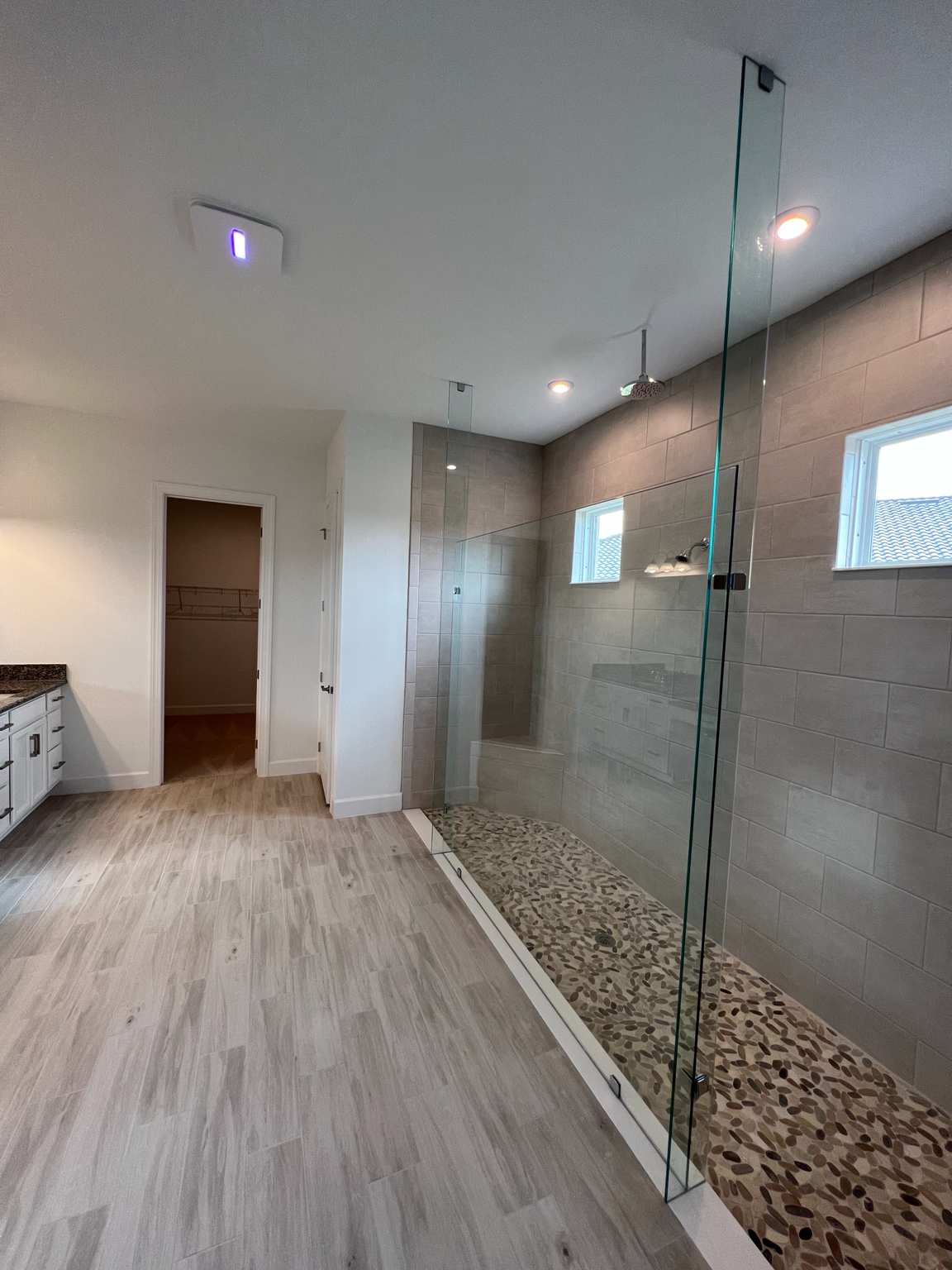 Modern bathroom with glass shower, pebble floor, and white vanity in a bright room