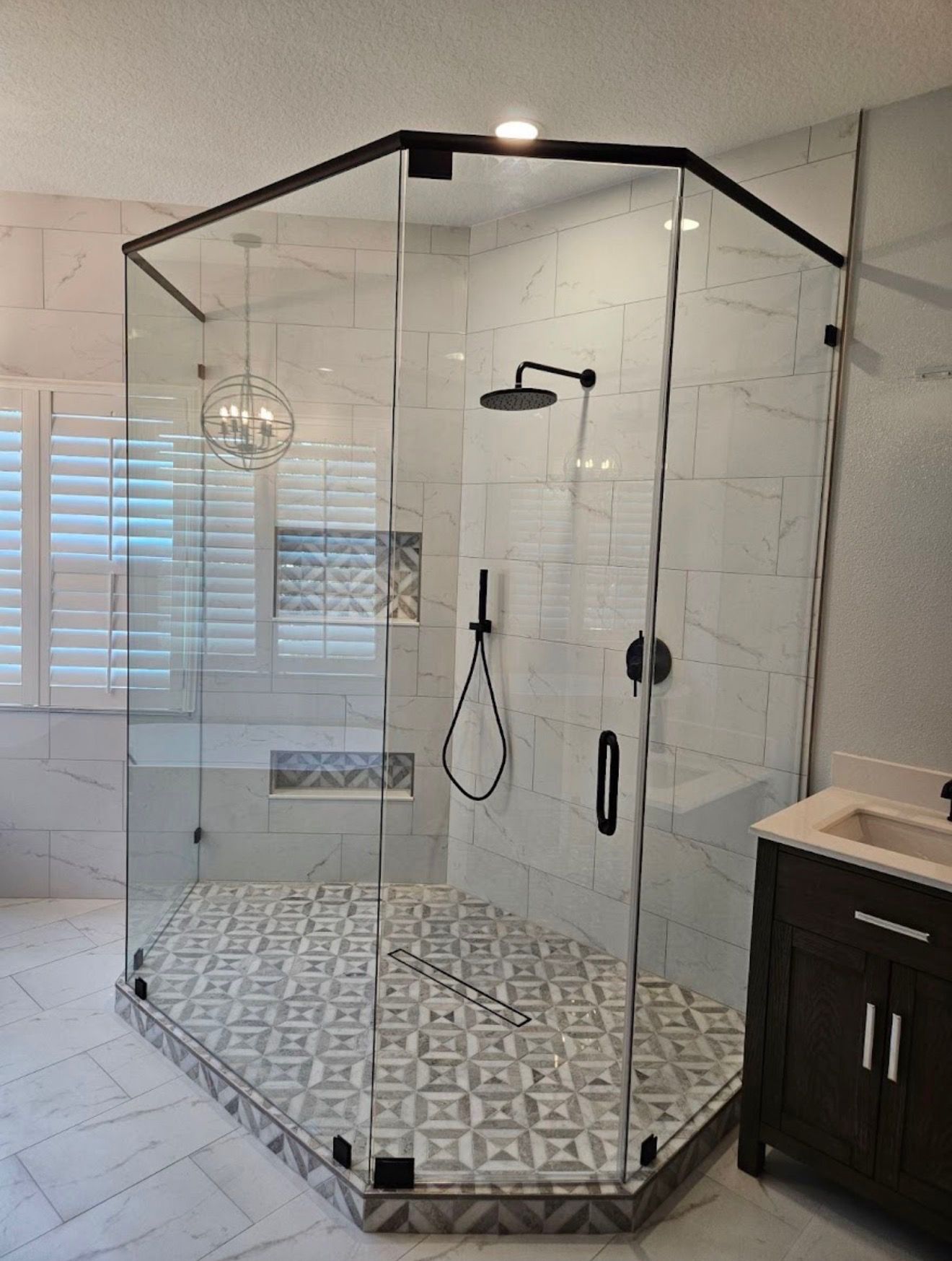 Glass corner shower with black trim and patterned tile floor in a modern bathroom