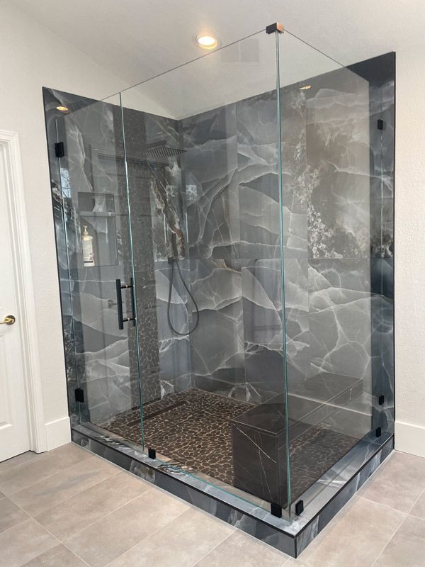 Modern glass walk-in shower with dark marble-pattern panels and tiled floor in a bathroom.