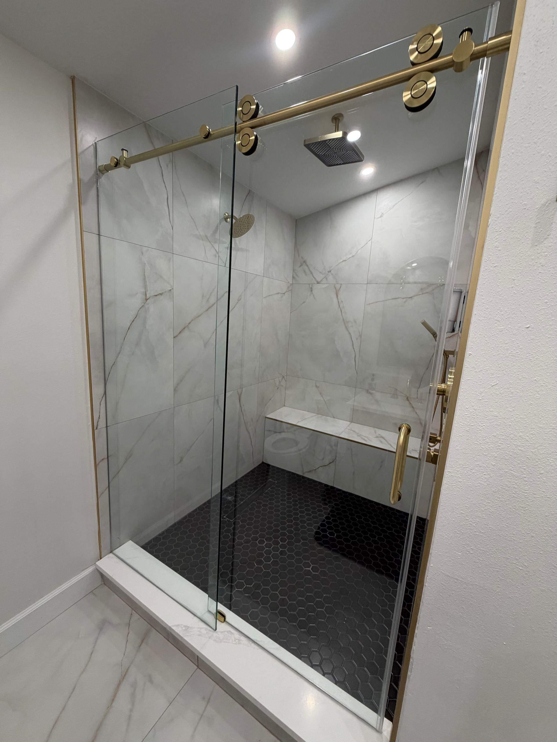 Glass shower enclosure with brown tile walls and a white pebble floor in a bathroom