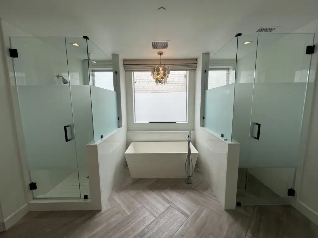 A symmetrical luxury bathroom with a freestanding bathtub between dual shower enclosures with matte black hardware and frosted center privacy band panels