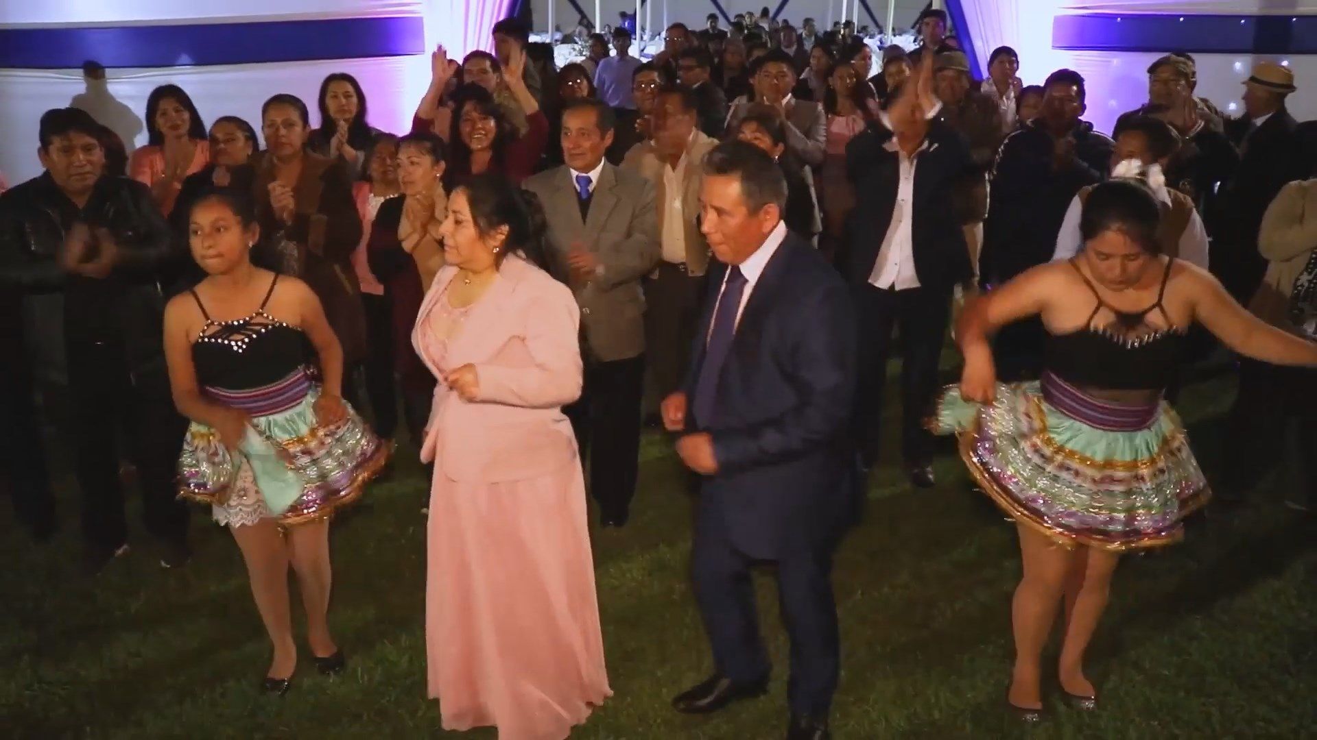 Actuación de danza con dos mujeres con faldas de colores, una mujer vestida de rosa y un hombre con traje en un escenario interior iluminado