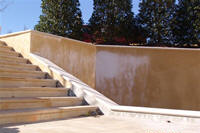Staircase leading up to a tan stucco wall. White discoloration on the wall, trees in background.