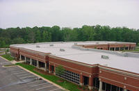 Brick building with flat white roof, green trees in background, overcast sky.