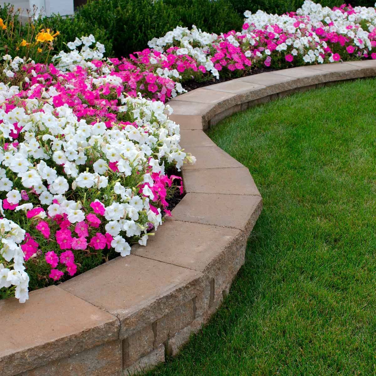 Curved stone garden border lined with pink and white flowers beside a green lawn