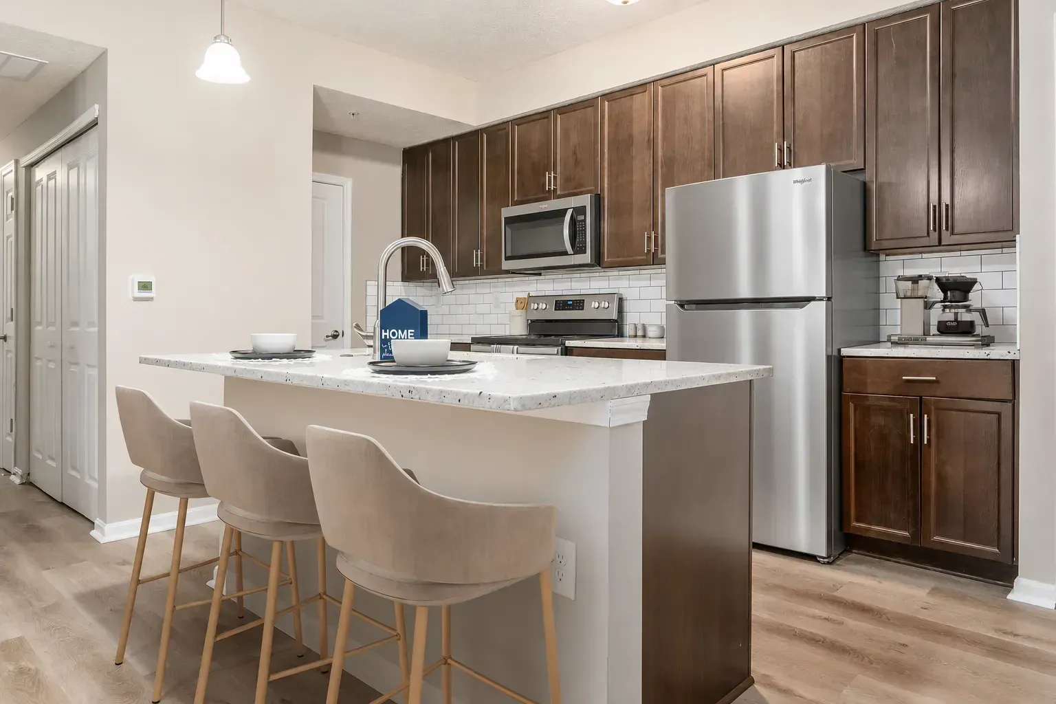 Modern kitchen with island, beige chairs, stainless steel appliances, and dark wood cabinets