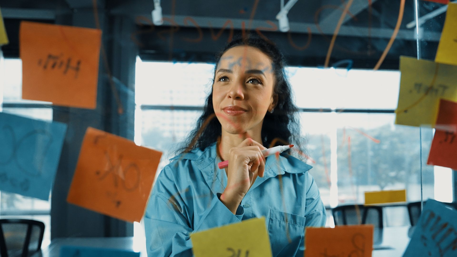A woman is looking at sticky notes on a glass wall.