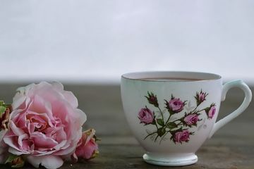 Pink rose beside a white teacup with floral design on a wooden surface