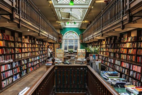 Symmetrical bookstore aisle with tall shelves of colorful books and a large arched window at the back