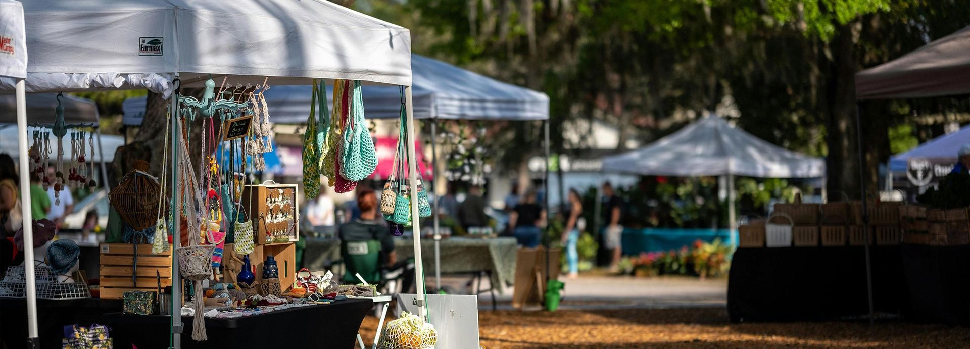 Outdoor market stalls with colorful crafts under white canopies in a sunny park