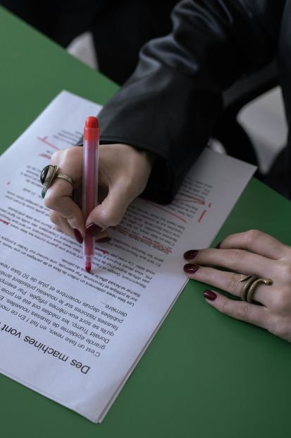 Hands signing a document with a red pen on a green table.