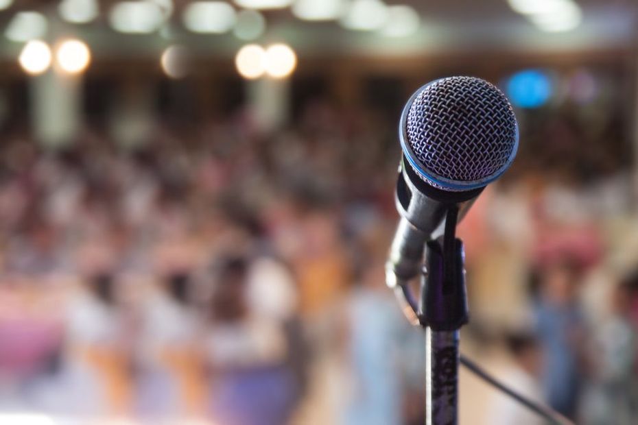 Microphone on a stand in front of a blurred audience at an indoor event