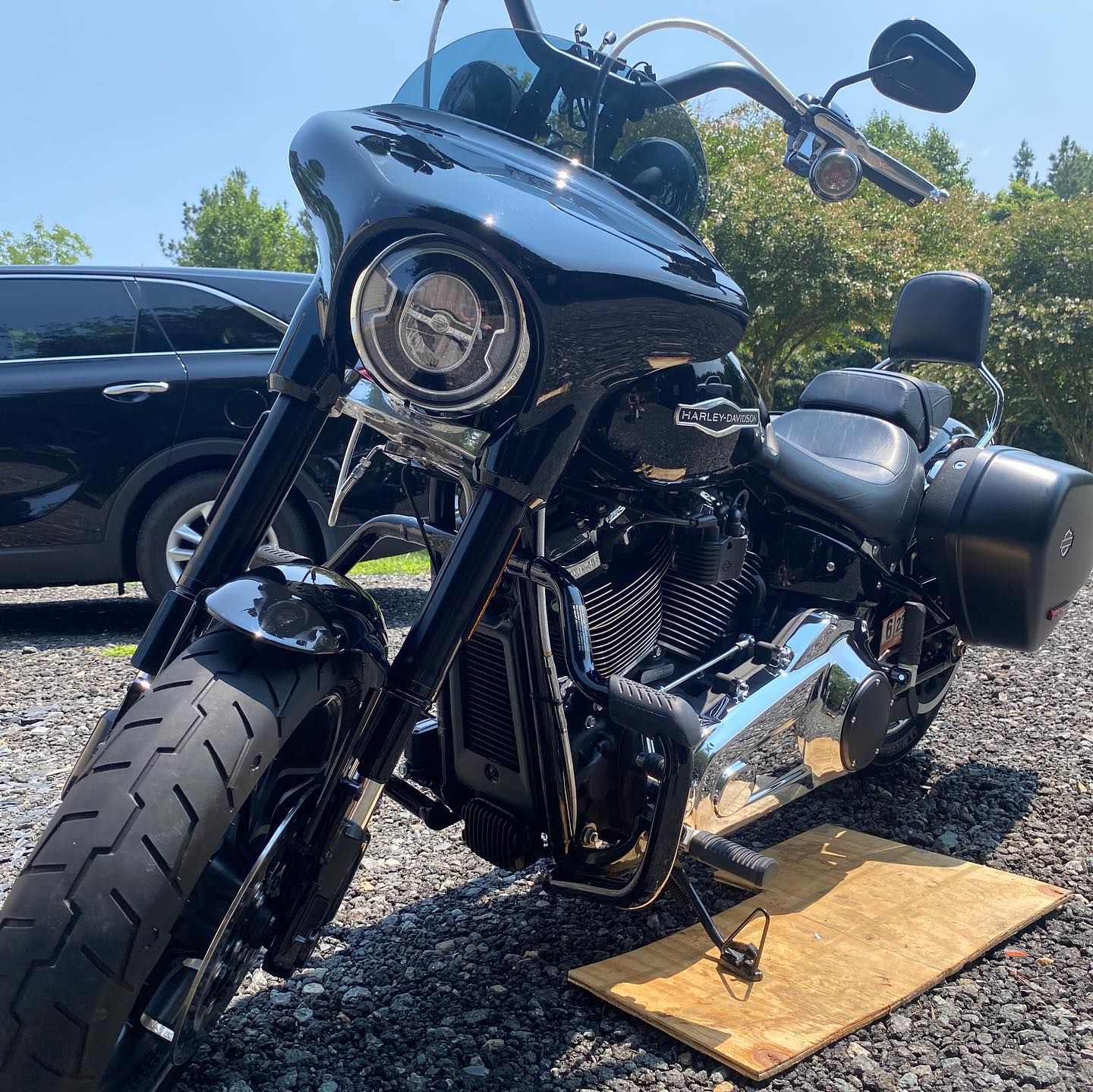 Black custom motorcycle parked outdoors on pavement beside a car, with a large front tire and chrome details