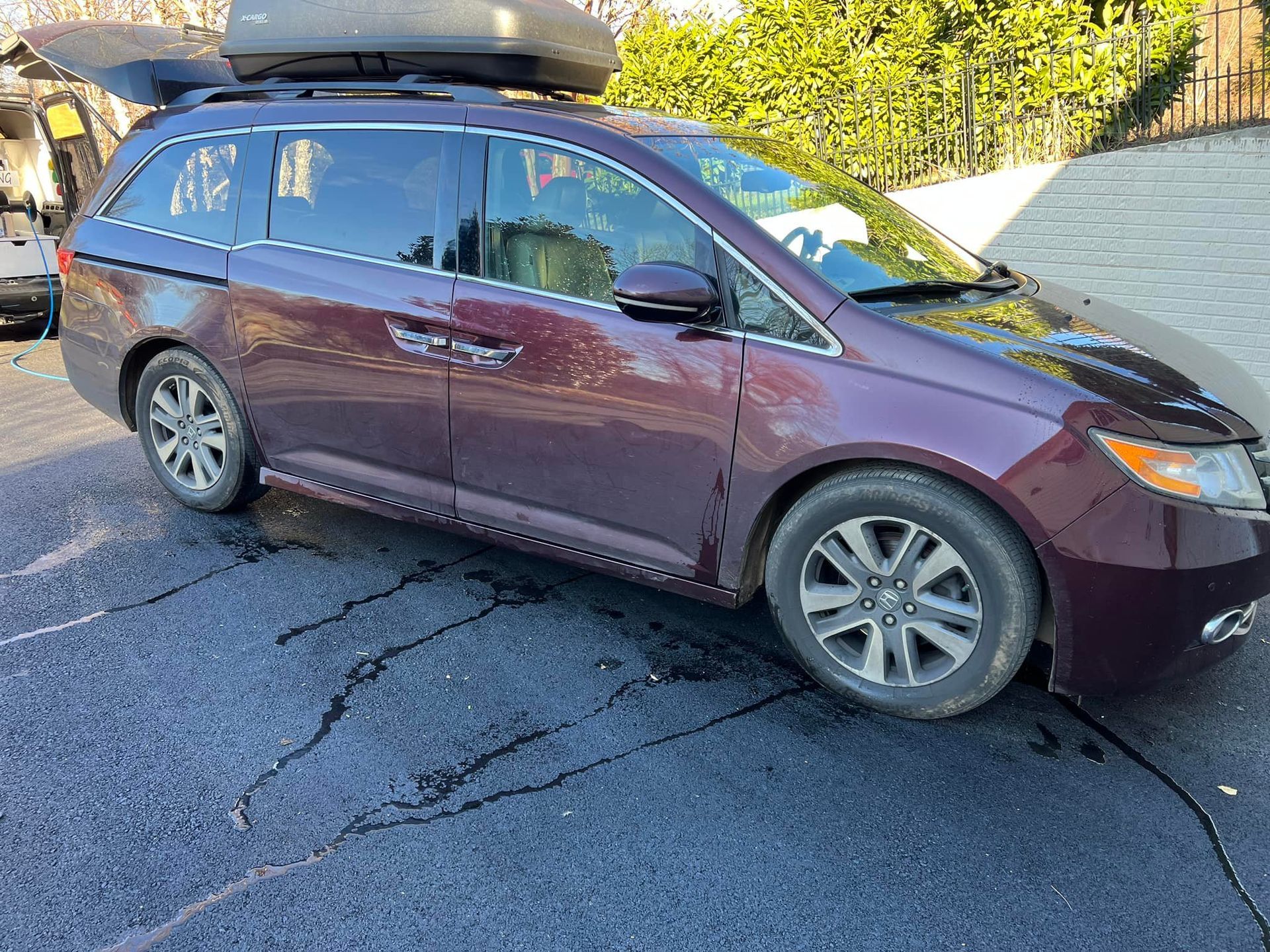 Maroon minivan parked on a cracked driveway with a roof cargo box attached.