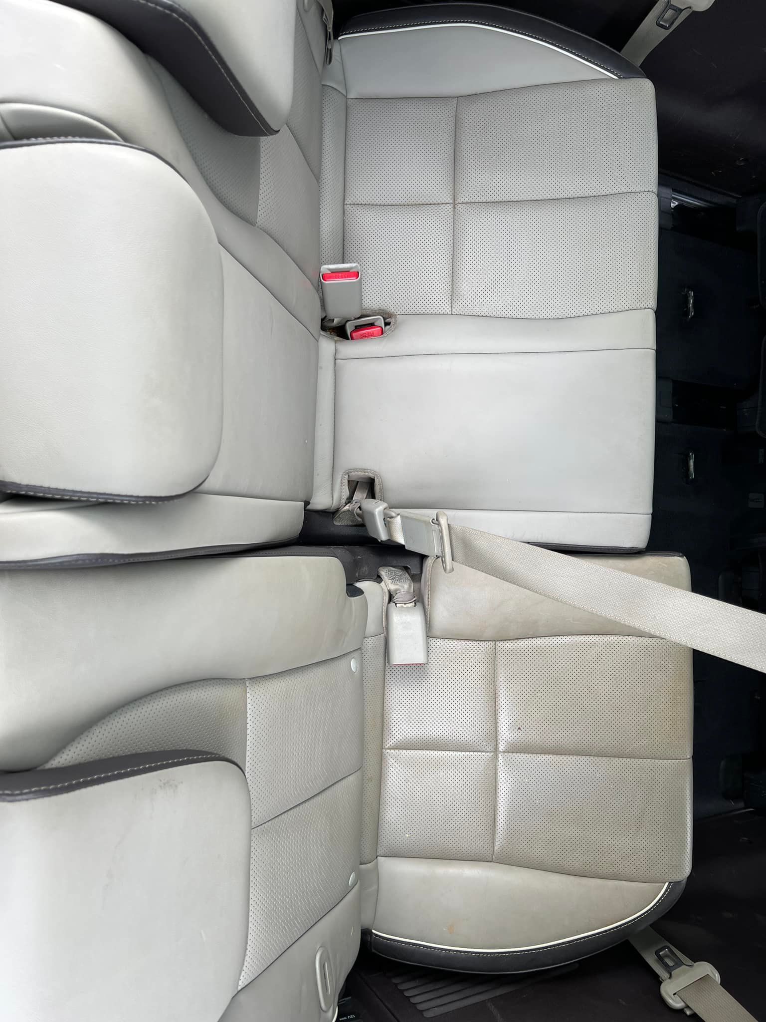 Top-down view of a car’s gray leather rear seats with seatbelts and a central armrest.