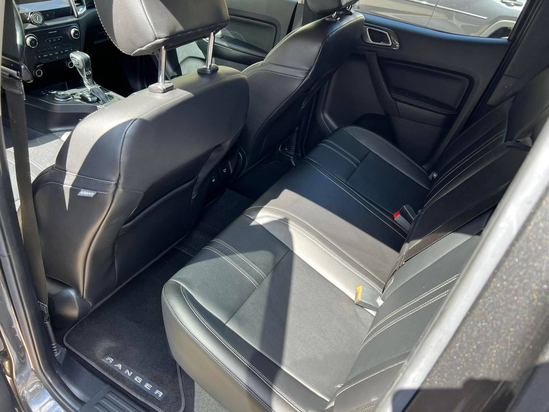Car interior with black leather back seat and visible front seat, viewed from the open rear door