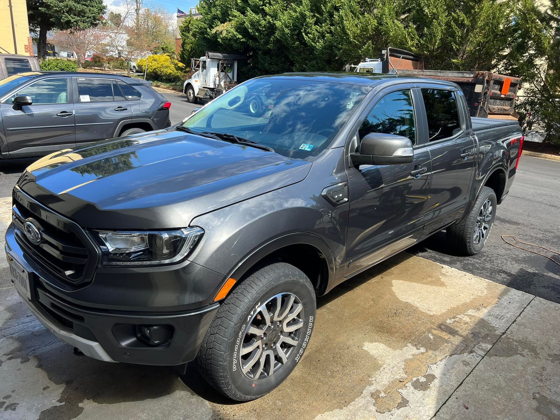 Gray pickup truck parked on a street, front-left view, with trees and other cars in the background