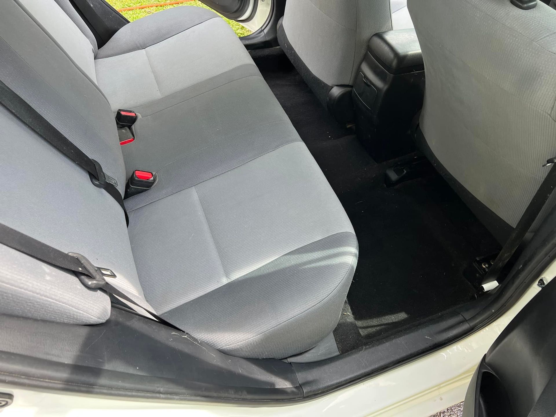 Rear seat of a car with gray upholstery and black floor mats, viewed from the open door