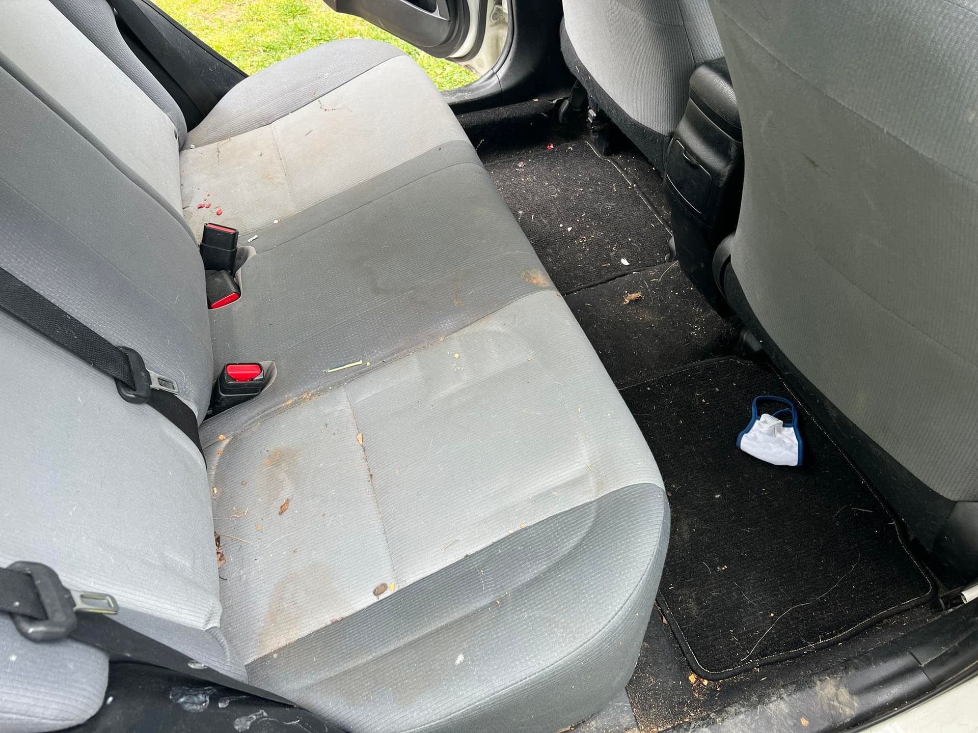 Dirty back seat and floor of a car with scattered crumbs and debris