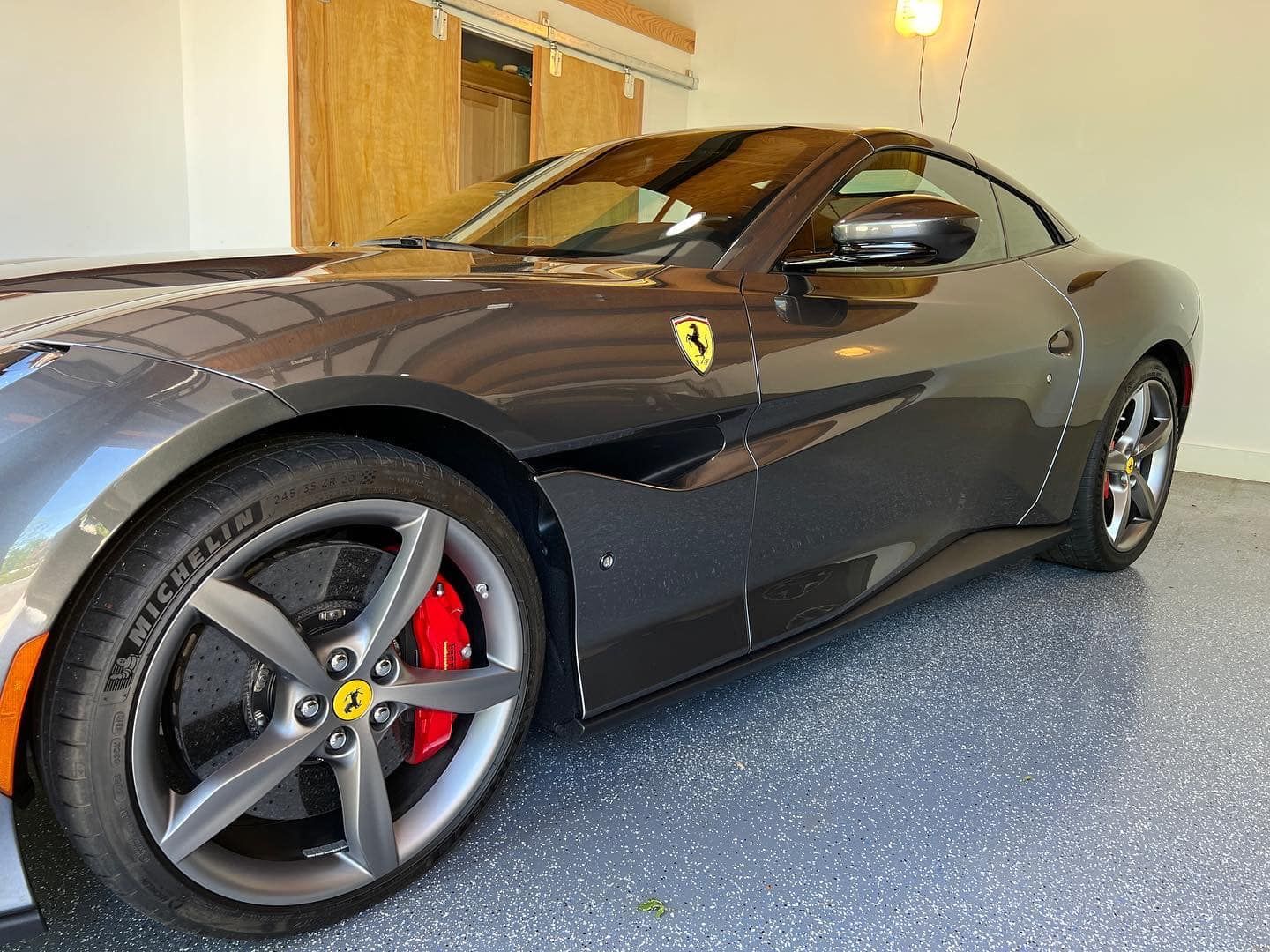 Black Ferrari sports car parked indoors with red brake calipers and a gray rim on display.